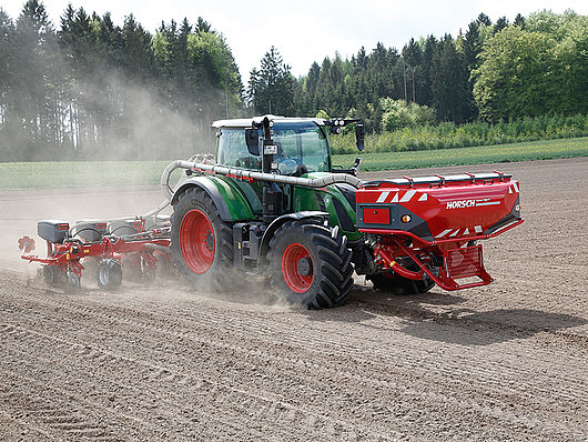 Ein Traktor, der Mais auf dem Feld sät und dabei Staub erzeugt