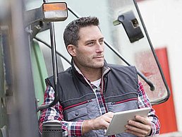 Mann auf Traktor mit iPad in der Hand blickt in die Ferne.