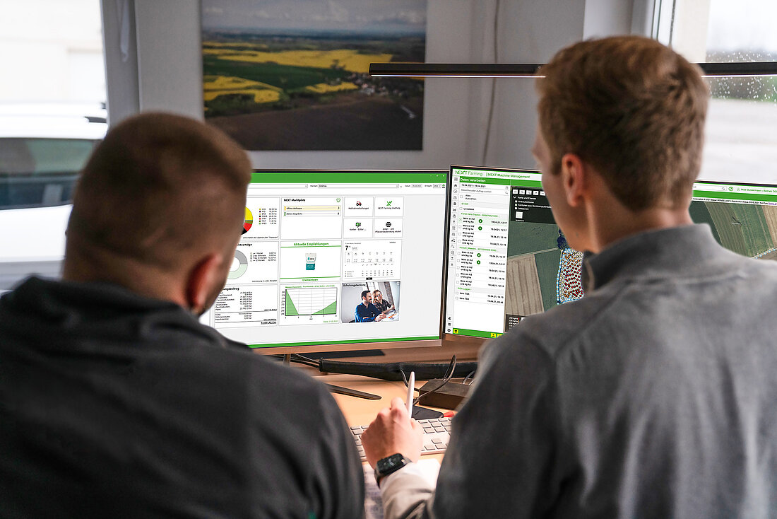 Zwei Landwirte sitzen vor zwei Computerbildschirmen, auf denen die NEXT Farming Software zu sehen ist